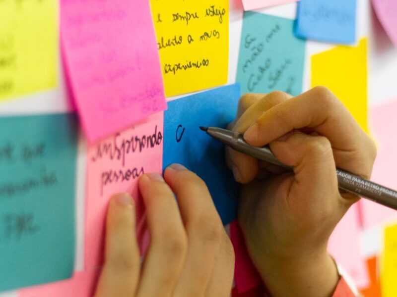 Hands writing on colorful sticky notes during a brainstorming session indoors.