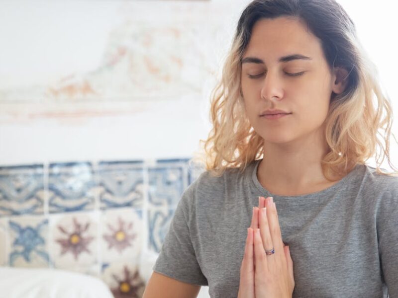 Peaceful woman meditating indoors, eyes closed, in a serene environment.