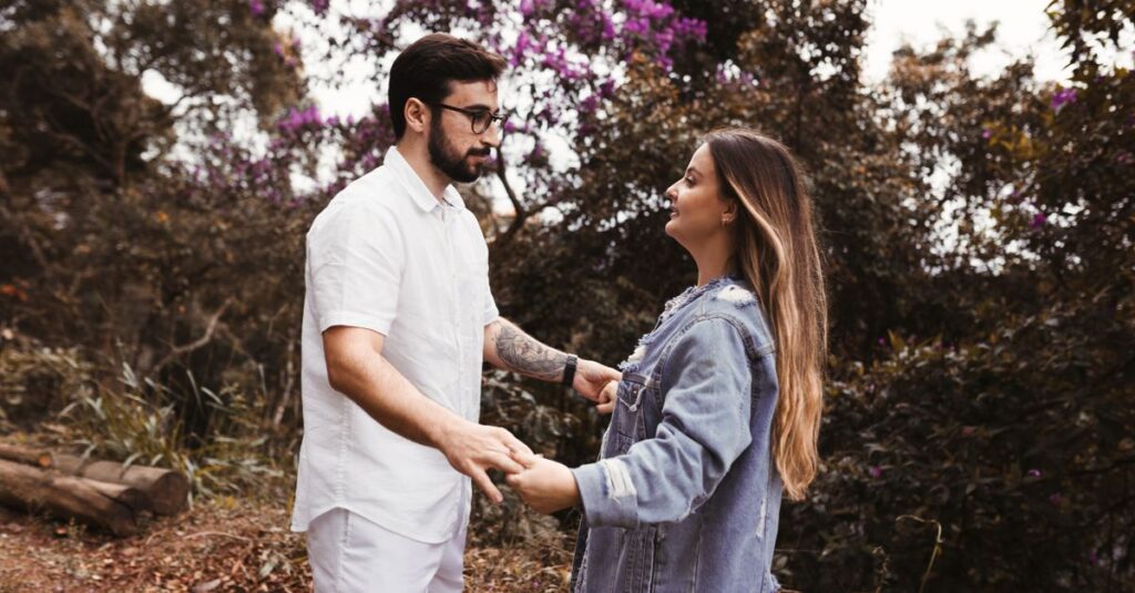 Como Cultivar a Autoconfiança em Relacionamentos Saudáveis 2 A young couple holding hands in a forest, surrounded by lush greenery and purple flowers.