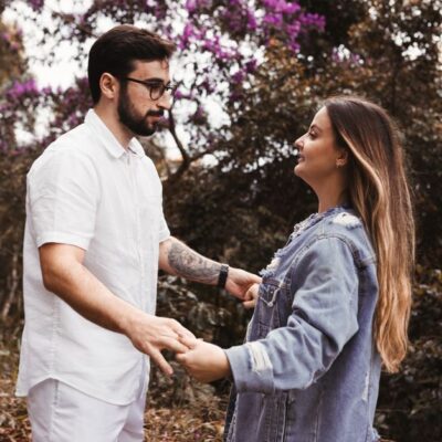 A young couple holding hands in a forest, surrounded by lush greenery and purple flowers.