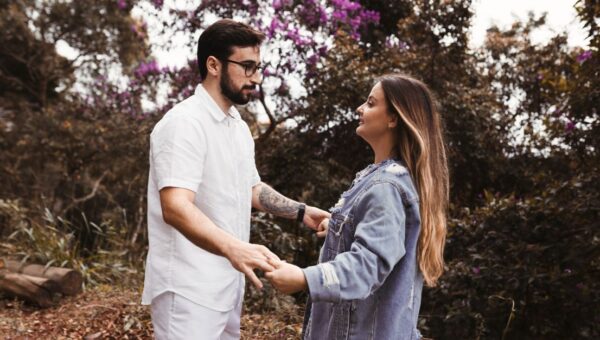 A young couple holding hands in a forest, surrounded by lush greenery and purple flowers.