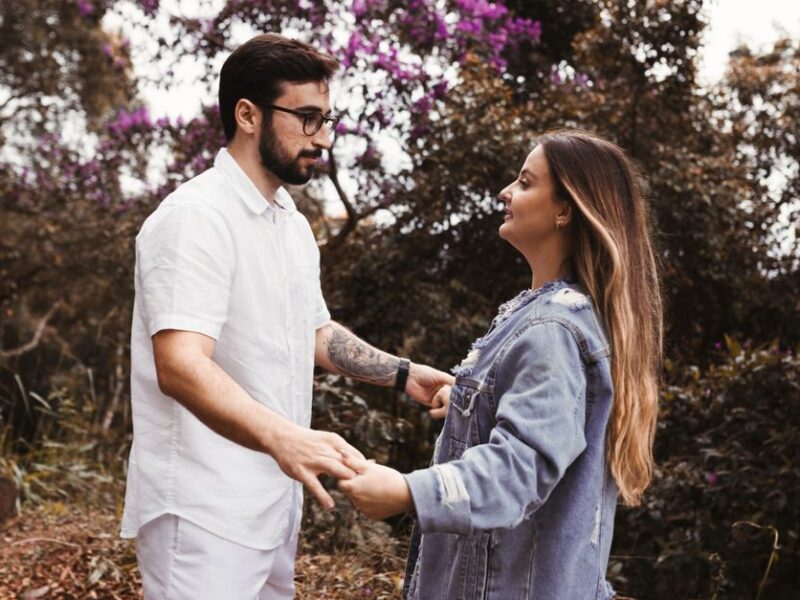 A young couple holding hands in a forest, surrounded by lush greenery and purple flowers.