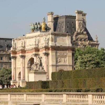 Sunny day at the Arc de Triomphe du Carrousel in Paris with people relaxing nearby.