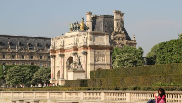 Sunny day at the Arc de Triomphe du Carrousel in Paris with people relaxing nearby.