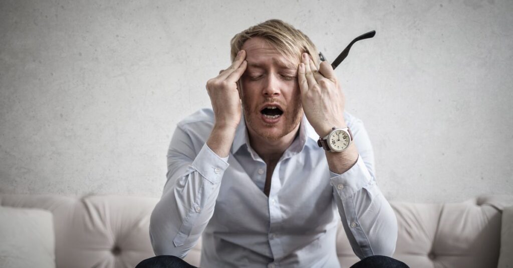 Stressed man sitting on couch, feeling overwhelmed and frustrated, expressing mental strain.