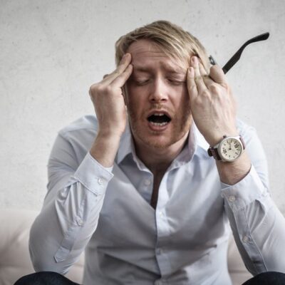 Stressed man sitting on couch, feeling overwhelmed and frustrated, expressing mental strain.
