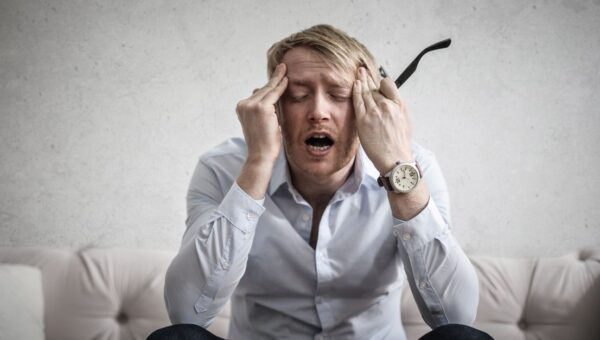 Stressed man sitting on couch, feeling overwhelmed and frustrated, expressing mental strain.