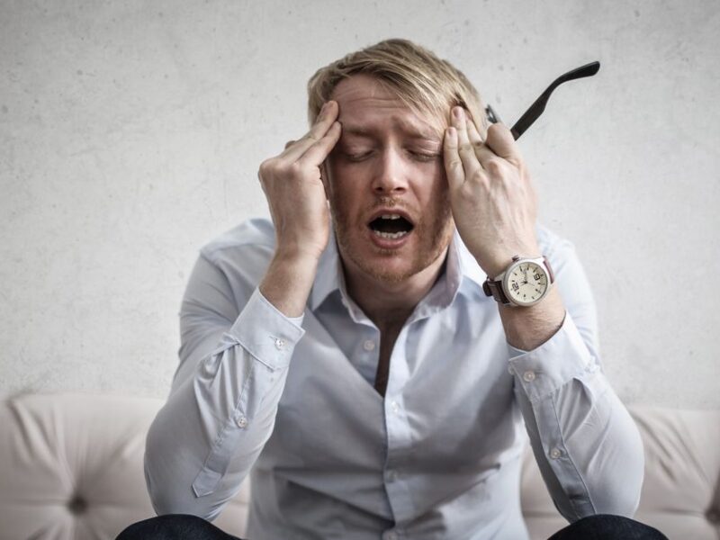 Stressed man sitting on couch, feeling overwhelmed and frustrated, expressing mental strain.