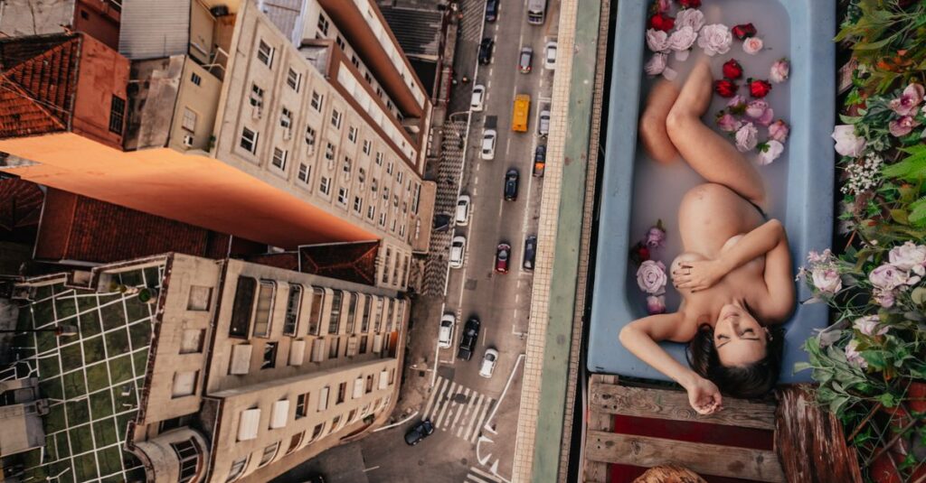 Como Viver a Maternidade com Criatividade e Leveza 2 Pregnant woman in a bathtub with flowers, high above the city street, offering a unique urban bath experience.