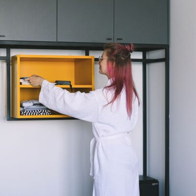 A woman in a bathrobe organizes a wardrobe in a modern hotel room.