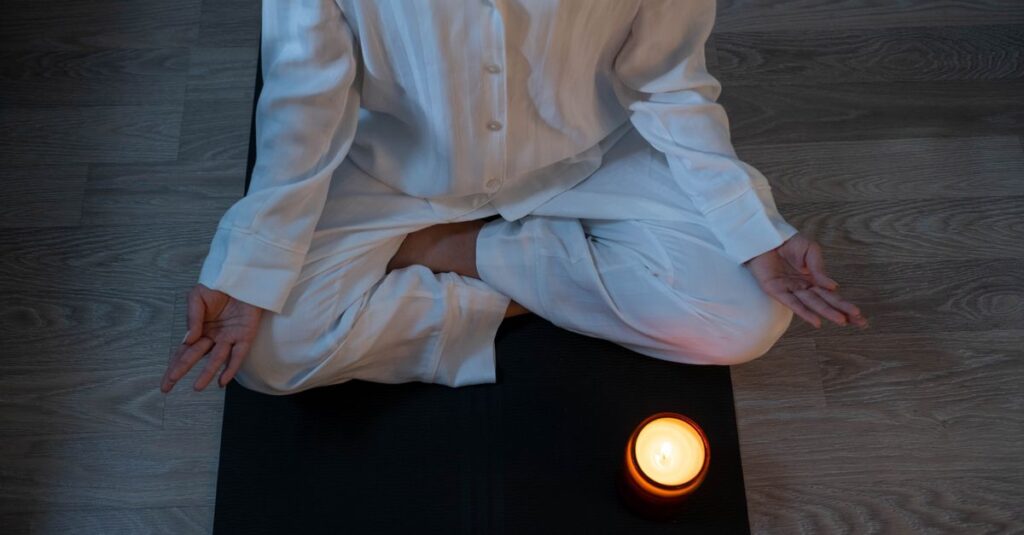 Serene meditation scene with a person in white pajamas and a glowing candle for relaxation.