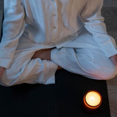 Serene meditation scene with a person in white pajamas and a glowing candle for relaxation.