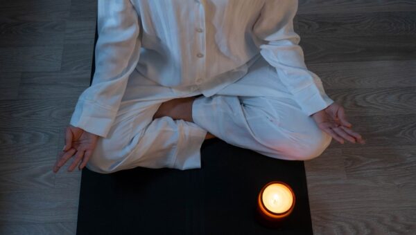 Serene meditation scene with a person in white pajamas and a glowing candle for relaxation.