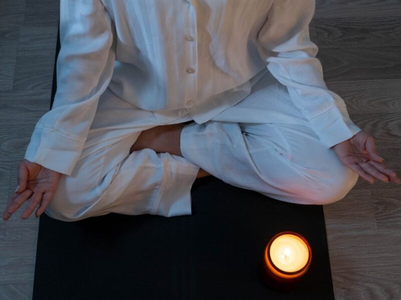 Serene meditation scene with a person in white pajamas and a glowing candle for relaxation.