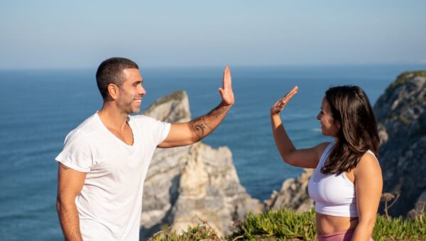 Fit couple in athletic wear high-fiving by the sea on a sunny day in Portugal.