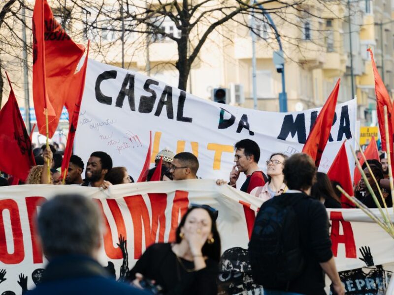 Group of people in a city staging a protest with banners and red flags during the day.