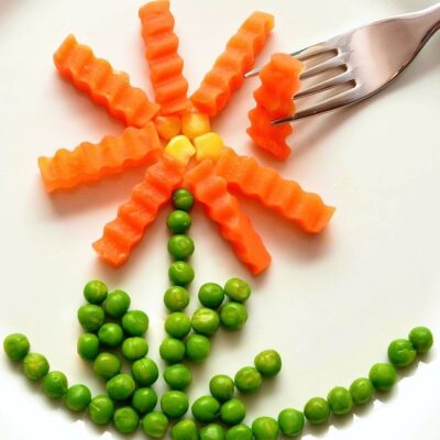 A playful flower made from carrots and peas on a white plate with a fork, showcasing creativity in food art.