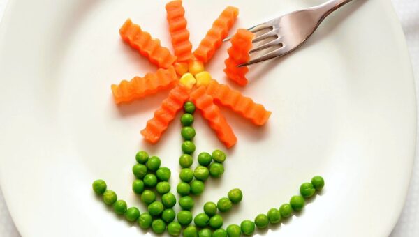 A playful flower made from carrots and peas on a white plate with a fork, showcasing creativity in food art.