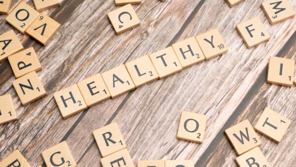 Wooden letter tiles arranged on a wooden surface spelling out 'healthy', symbolizing wellness.