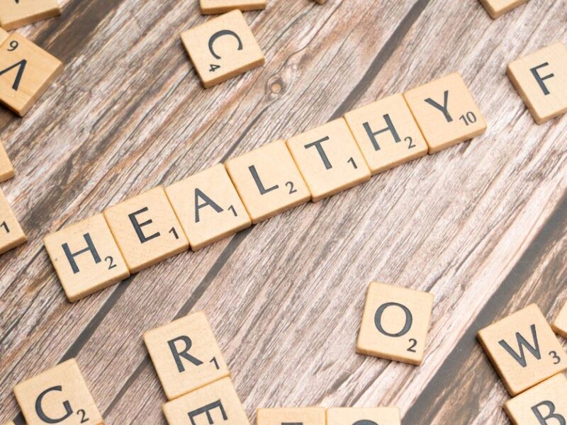 Wooden letter tiles arranged on a wooden surface spelling out 'healthy', symbolizing wellness.
