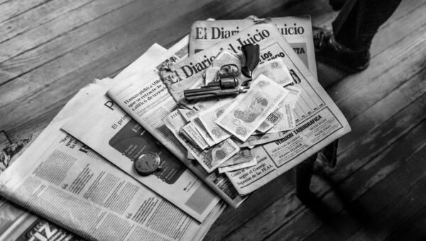 Black and white image featuring currency, newspapers, and a revolver on a wooden surface.