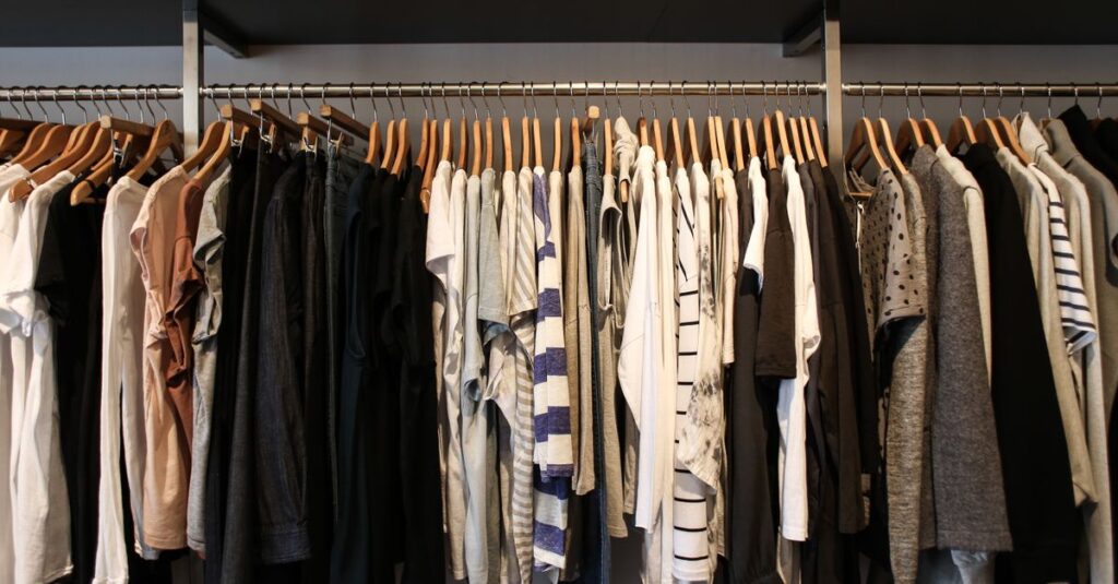 Como Criar um Armário-Cápsula Prático e Sustentável 2 Diverse range of fashionable clothes on wooden hangers in a boutique setting.