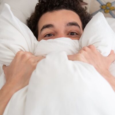 A young man relaxing in bed with a pillow, enjoying a peaceful morning indoors.
