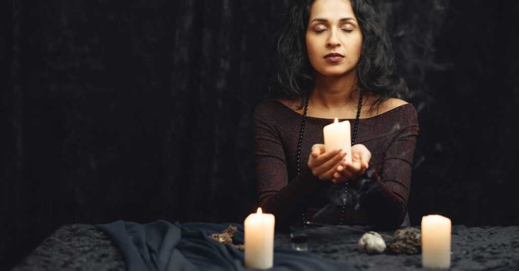 A woman meditates with candles in a dimly lit room, creating a serene atmosphere.