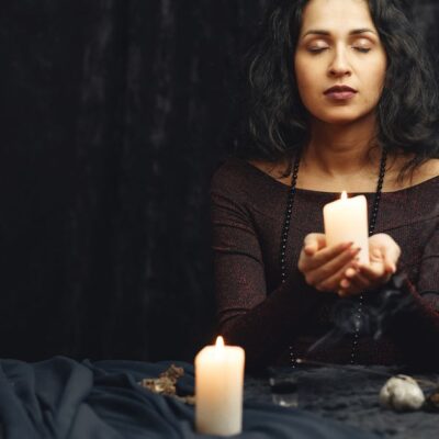 A woman meditates with candles in a dimly lit room, creating a serene atmosphere.