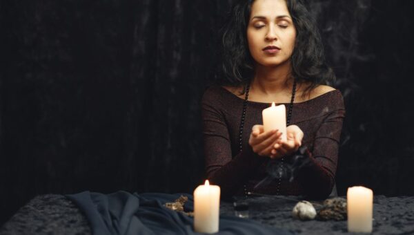 A woman meditates with candles in a dimly lit room, creating a serene atmosphere.