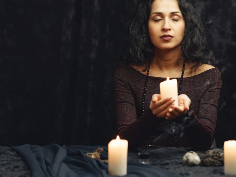 A woman meditates with candles in a dimly lit room, creating a serene atmosphere.