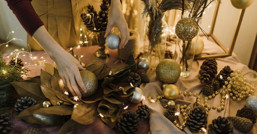 Hands arranging Christmas baubles and pine cones on a festive decorated table.