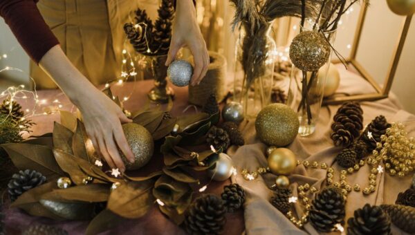 Hands arranging Christmas baubles and pine cones on a festive decorated table.
