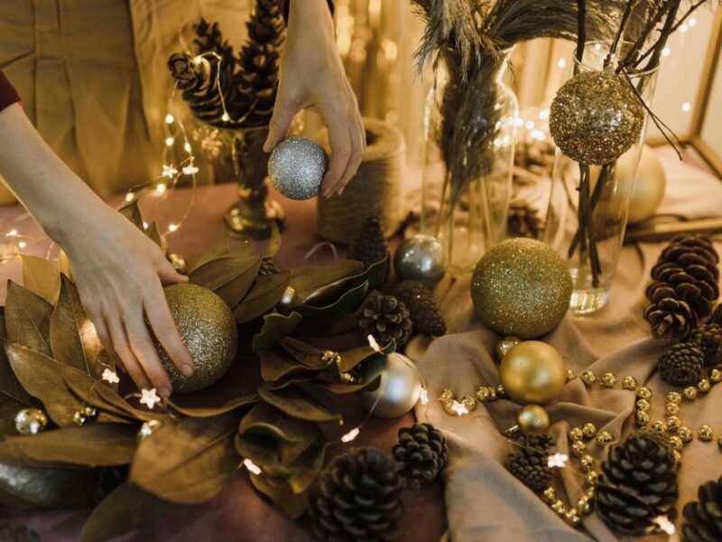 Hands arranging Christmas baubles and pine cones on a festive decorated table.