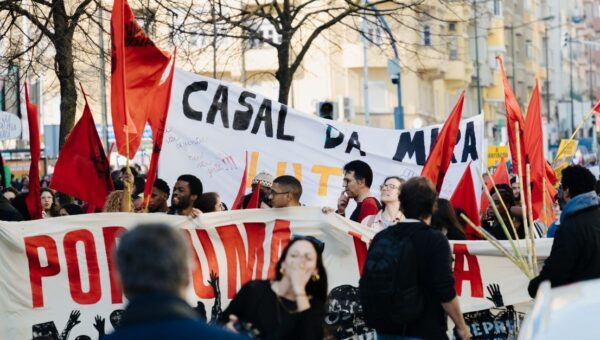Group of people in a city staging a protest with banners and red flags during the day.