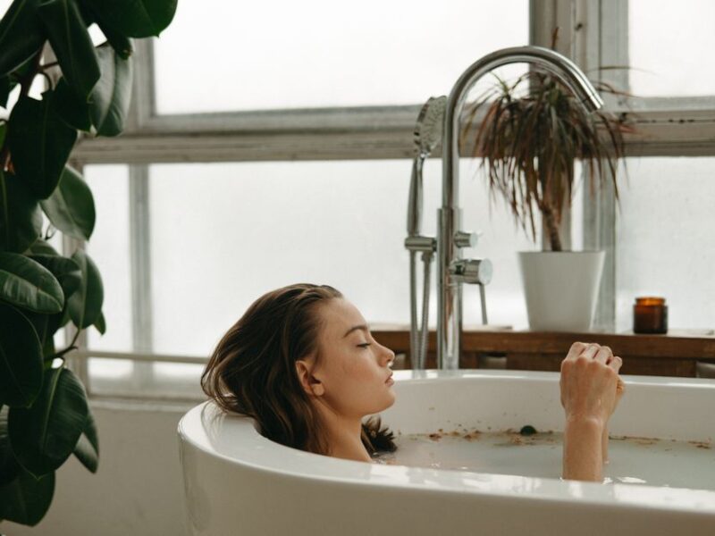 A woman peacefully soaking in a bathtub surrounded by plants and candles, embracing tranquility.