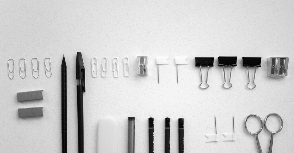 Como Lidar com o Perfeccionismo e Encontrar sua Leveza 2 Neatly arranged office supplies including scissors, pens, and clips on a plain white background.