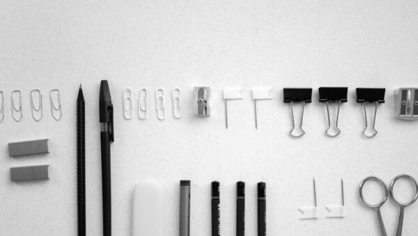 Neatly arranged office supplies including scissors, pens, and clips on a plain white background.