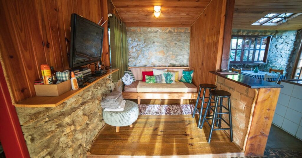 Interior of rustic house with counter placed near sofa with cushions and TV hanging on wooden wall near various supplies