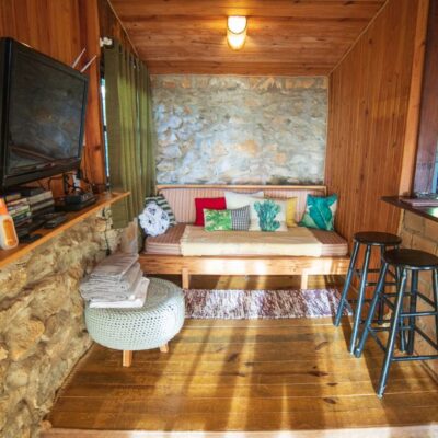 Interior of rustic house with counter placed near sofa with cushions and TV hanging on wooden wall near various supplies