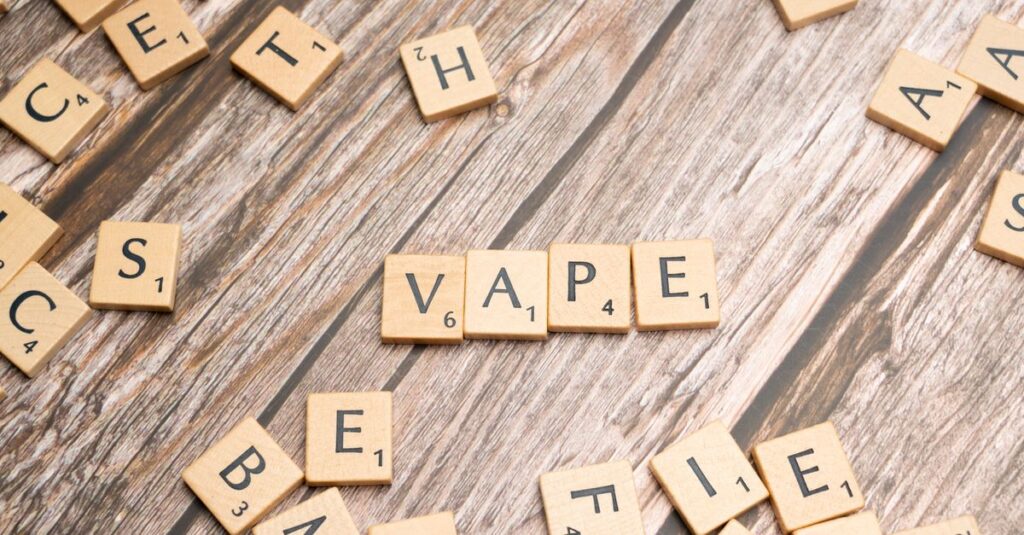 Wooden scrabble tiles with the word 'vape' on a textured wooden surface.