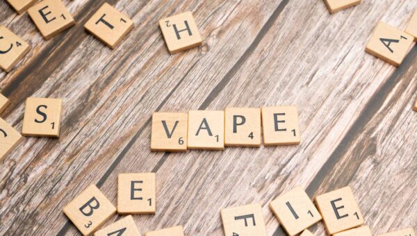 Wooden scrabble tiles with the word 'vape' on a textured wooden surface.
