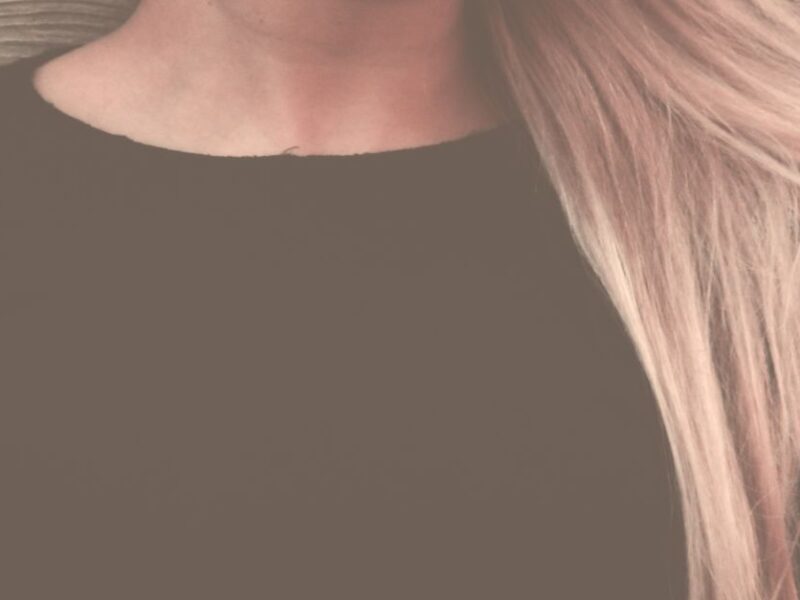 Close-up portrait of a woman with long, flowing blonde hair against a textured background.