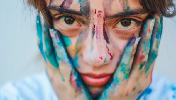 Close-up portrait of a young girl with a painted face and hands, showcasing creativity.