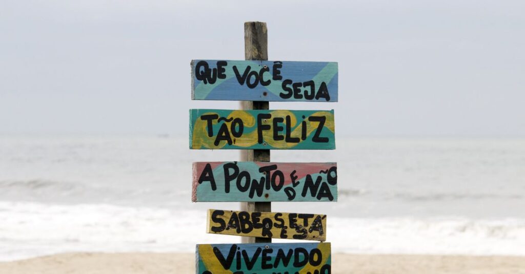Colorful beach sign in Guaratuba, Brazil with motivational text against ocean waves.