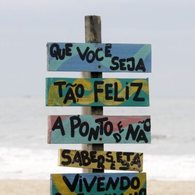 Colorful beach sign in Guaratuba, Brazil with motivational text against ocean waves.
