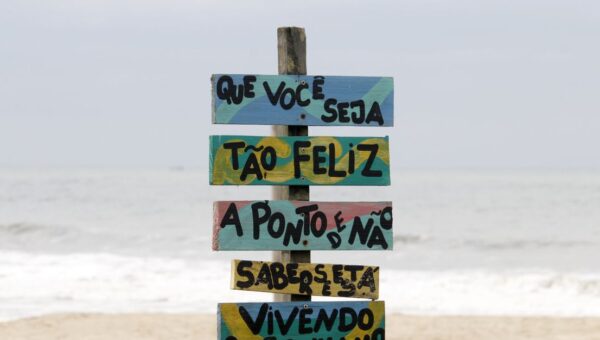 Colorful beach sign in Guaratuba, Brazil with motivational text against ocean waves.