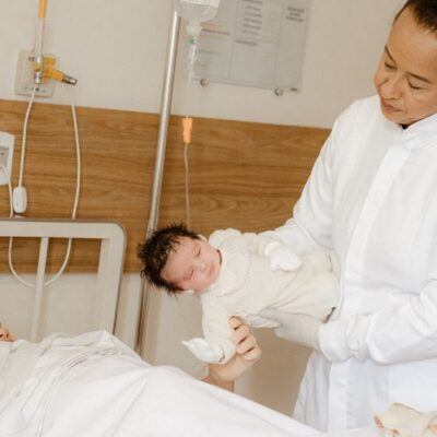 A doctor assists a new mother with her newborn baby in a hospital room setting.
