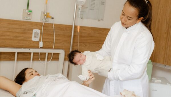 A doctor assists a new mother with her newborn baby in a hospital room setting.