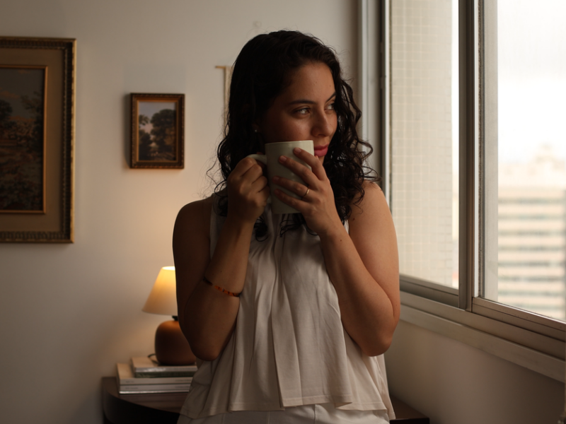 Young woman gazing out window with coffee, enjoying morning indoors.